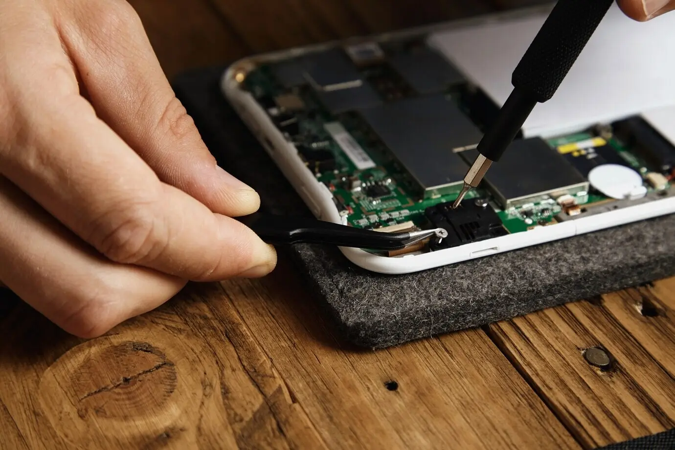 Ein Meister verwendet spezielle Werkzeuge, um ein elektronisches Gerät vorsichtig zu zerlegen: Zange und Bit-Schraubendreher.